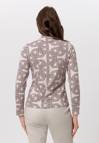 Top met lange mouwen in beige stof met een gedurfd bordeauxrood geometrisch patroon, een losse pasvorm en een gladde textuur, eindigend bij de taille.