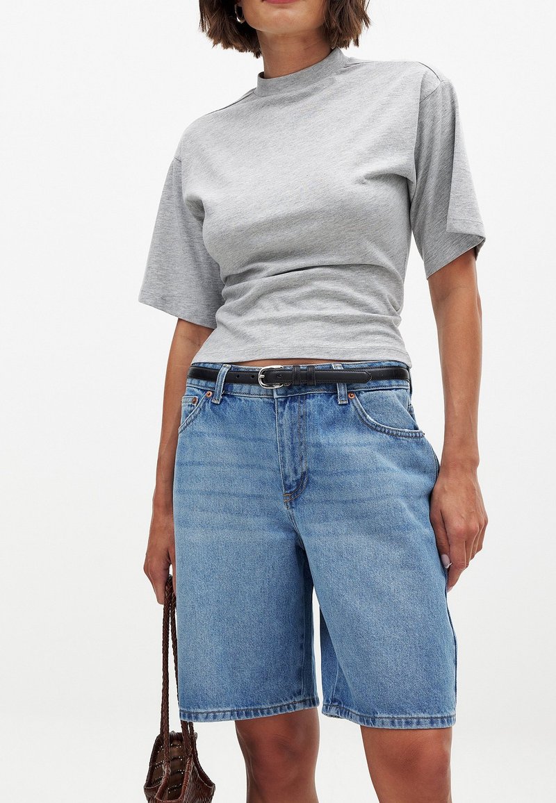 Pelēks īsām piedurknēm tops, apvienots ar ziliem džinsu šortiem, ar standarta piegriezumu, jostas cilpām un priekšējām kabatām. Strukturēta kokvilnas audums.