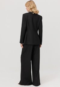 Czarny garnitur z dopasowaną marynarką z taliowanym tyłem oraz spodniami o szerokich nogawkach. Gładki materiał z ozdobnymi guzikami na rękawach.