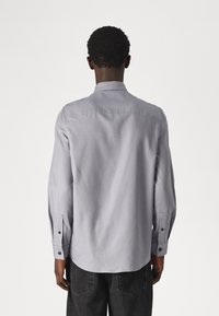 Lichtgrijs overhemd met lange mouwen, standaard kraag, knoopmanchetten en een gladde textuur, gestyled met een subtiele glans.