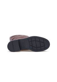Brauner Lederstiefel, der auf der Seite liegt und eine schwarze Gummisohle mit Grip-Muster und niedrigem Absatz zeigt.