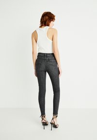 Crne skinny traperice visokog struka s blagim izbljeđivanjem, dva stražnja džepa i bešavni dizajn stražnjeg dijela, uparene s prilagođenim bijelim majicom bez rukava.
