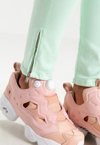 Baskets roses avec des superpositions texturées et des découpes, ornées de deux boutons blancs et d'une semelle épaisse blanche. Jean vert menthe avec des détails zippés.