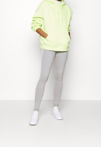 Neon grön huvtröja med framfickor, i kombination med grå leggings med vita sidosträck. Vita sneakers fulländar outfiten.