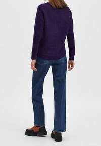 Suéter morado de punto texturizado con escote redondo, combinado con jeans de mezclilla azul de corte holgado y zapatos plataforma negros con detalles en marrón.