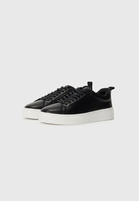 Scarpe da ginnastica in pelle nera con finitura liscia, dotate di suola in gomma bianca, punta rotonda e chiusura con lacci, con un inserto posteriore per il sollevamento.