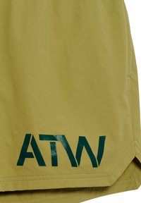 Żółta tkanina z ciemnozielonym stylizowanym logo "ATW" nadrukowanym blisko brzegu, z podwójnymi szwami i małym bocznym rozporkiem.