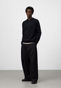 Svart stickad långärmad tröja med halvmidja och krage, tillsammans med lösa, vida svarta byxor. Slät tyg, minimalistisk design.