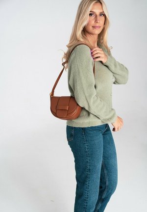 Brązowa skórzana torba na ramię o zakrzywionym kształcie, z fakturowanym wykończeniem i przednią klapką. Modelka ma na sobie zielony sweter i niebieskie dżinsy.