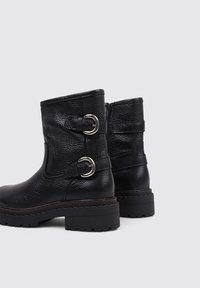Bottines noires en cuir avec une finition texturée, des accents à double boucle et une semelle épaisse avec un léger talon.
