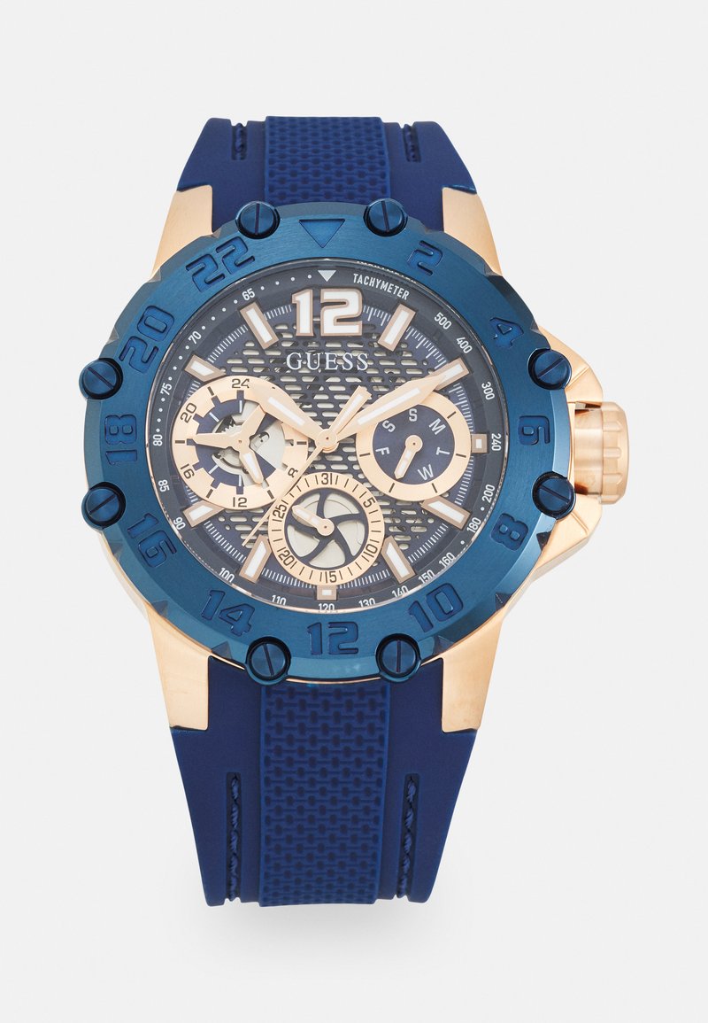 Orologio in silicone blu con cinturino testurizzato, accenti dorati, quadrante circolare, indicatori delle ore bianchi, sottodial dorati e scala tachimetrica.