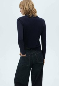 Temno modra dolgi rokav pulover z okroglim izrezom, v kombinaciji s temno denim širokimi hlačami, ki imajo dve zadnji žepu in kontrastni šiv.