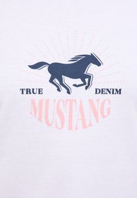 White cotton t-shirt featuring a navy horse silhouette and the text "TRUE DENIM MUSTANG" in pink and black, with sunburst patterns.
