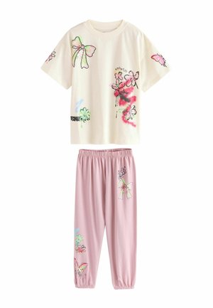 Bawełniany zestaw składający się z dwóch elementów, zawierający bluzkę z krótkim rękawem w kremowym kolorze z kolorowymi nadrukami w kwiaty i kokardki, połączoną z różowymi spodniami na elastycznej talji.