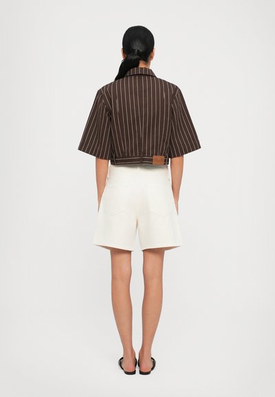 Brown striped cropped shirt with short sleeves, paired with white shorts. Notable brown leather tag at the back of the shirt.