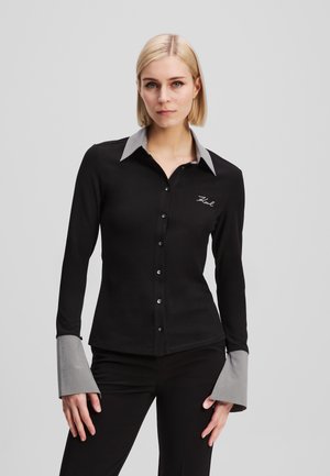 Black long-sleeve shirt with a gray collar and cuffs, featuring a button-down front and embroidered detail on the chest. Smooth fabric.