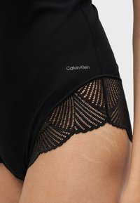 Μαύρα εσώρουχα Calvin Klein με δαντέλα στο μηρό, που δείχνουν υφή δέρματος και λεπτομέρειες ραφών στο ύφασμα.