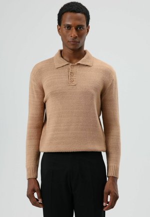 Beige gebreide trui met een kraag, voorzien van vier knopen en geribbelde manchetten. De stof heeft een zachte textuur en een losse pasvorm.