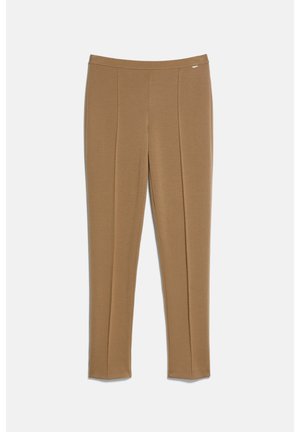 Pantalon marron slim-fit longueur cheville avec coutures visibles à l'avant et petit logo métallique près de la ceinture sur fond clair.