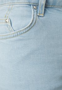 Ανοιχτό μπλε τζιν ύφασμα με υφή, που διαθέτει μπροστινή τσέπη και μεταλλικές λεπτομέρειες, συμπεριλαμβανομένου ενός κατόπτρου και κουμπιού.