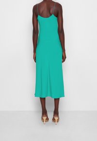 Une robe sans manches, longue jusqu'au sol, en tissu teal vif avec un corsage ajusté et une jupe évasée, dotée de fines bretelles et d'une texture lisse.