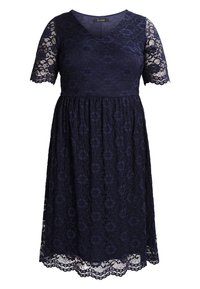 Granatowa koronkowa sukienka z krótkim rękawem, dekoltem w serek i rozkloszowanym dołem. Posiada kwiatowe wzory oraz falbaniaste wykończenie brzegu.