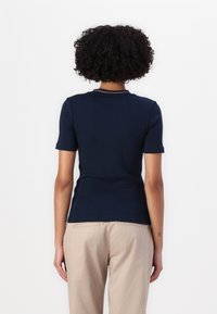 Top scurt cu mâneci scurte de culoare albastru închis, cu o textură ribbed și un decolteu rotund, având un accent contrastant cu dungi. Design ajustat.