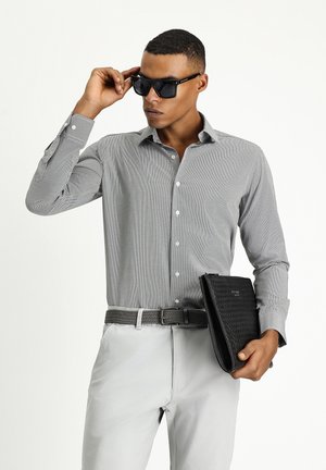Camisa de botones a rayas grises, de manga larga, con botones blancos, acompañada de un bolso negro texturizado y un cinturón trenzado gris, llevada con gafas de sol.