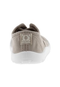 Zapato deslizante de lienzo beige con suela de goma blanca, que presenta una etiqueta de logo en la parte posterior y paneles laterales elásticos para un fácil calzado.