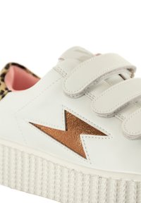 Baskets blanches en cuir avec un accent en éclair cuivré, des bandes velcro et une semelle blanche texturée. L'intérieur présente un revêtement rose avec un motif léopard.