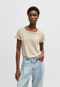 T-shirt beige a maniche corte in un tessuto testurizzato, con una scollatura ampia e un taglio rilassato, abbinato a jeans azzurri a vita alta.