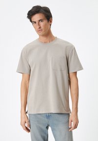 Beige bomulds t-shirt med rund halsudskæring, korte ærmer og lomme på venstre bryst. Blød struktur, afslappet pasform og lige afslutning.