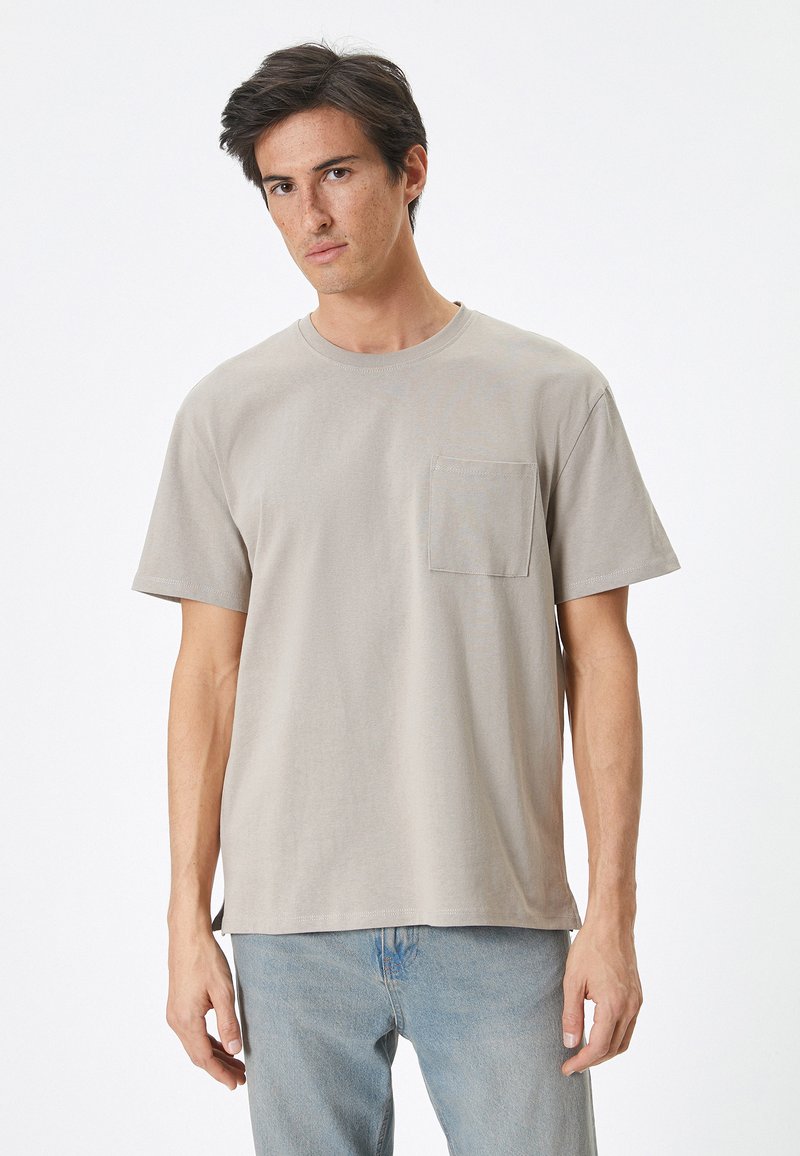 Camiseta de algodón beige con cuello redondo, mangas cortas y bolsillo en el pecho izquierdo. Textura suave, corte relajado y dobladillo recto.
