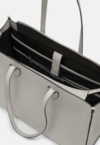 Sac fourre-tout en cuir gris clair avec intérieur noir. Dispose de deux poignées, d'une fermeture éclair et de plusieurs poches internes pour l'organisation.