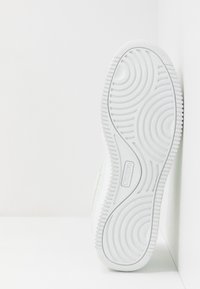 Weißer Gummisneaker mit wellenförmigem Profil und strukturierten Rändern; enthält Markenlogo an der Seite.