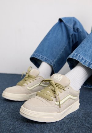 Beige semskinnesko med lysegrønne detaljer og snøring. Prentet "VANS"-logo på tungen. Teksturet gummisåle og flat hæl.