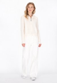 Crème geknoopte cardigan met een textuurpatroon, gecombineerd met witte wijde broek en witte sneakers.