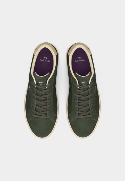 Ζευγάρι σκούρα πράσινα αθλητικά παπούτσια με κορδόνια, με κρέμ χρωματιστές λεπτομέρειες και μωβ εσωτερικές σόλες, φωτογραφημένα από πάνω σε απλό φόντο.