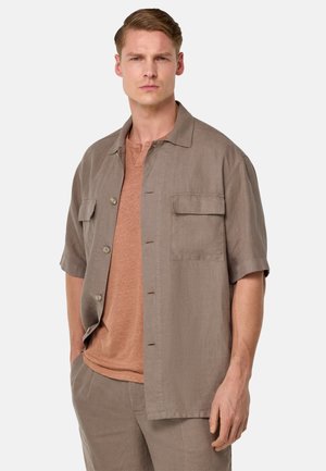 Short-sleeve brown linen shirt with a collar, two front pockets, and a smooth texture, worn over a light brown t-shirt.