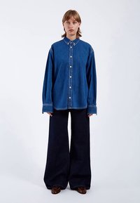 Denim shirt with a classic collar, buttons down the front, and long sleeves. Paired with wide-leg dark denim trousers.
