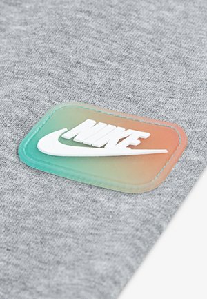 Weißes Nike-Logo auf einem rechteckigen, verlaufsförmigen Patch von Grün zu Orange, auf hellgrauem strukturiertem Stoff gestickt.