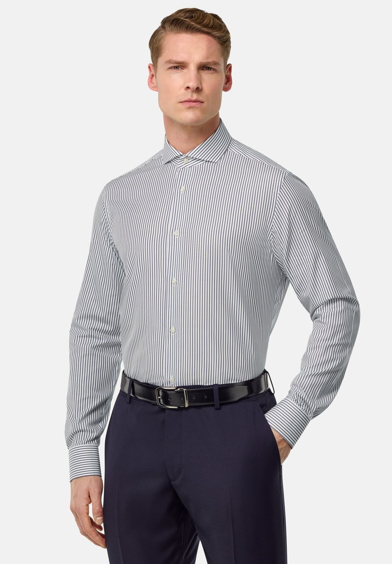Gestreiftes Hemd in Weiß und Marineblau, mit taillierter Passform, Button-Down-Kragen, langen Ärmeln mit geknöpften Manschetten. Kombiniert mit dunklen Hosen.