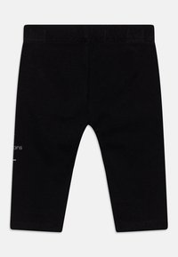 Svarta bomullstights med snug fit, elastisk midja och tryckt textdetalj på vänster sida. Slät textur, inga mönster.
