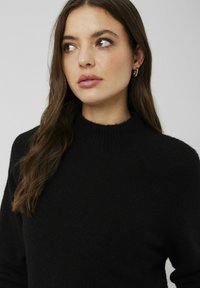 Pull noir en tricot doux, avec un col montant à côtes et des manches raglan. Aucun motif ou décoration visible.