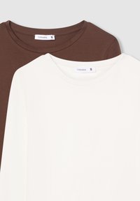 Due magliette a maniche lunghe con collo rotondo, una marrone e una bianca, di taglia piccola, etichettate Terranova, sovrapposte su uno sfondo grigio chiaro.