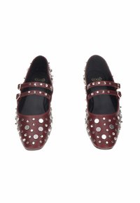 Scarpe Mary Jane di un rosso scuro con doppie cinghie, decorate con vari borchie e punte d'argento, mostrate dall'alto su uno sfondo bianco.