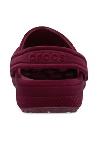 Bordowe Crocs z paskiem z tyłu, wykonane z miękkiego, gumowanego materiału. Posiadają teksturowaną podeszwę i gładką górną powierzchnię. Prosty design bez wzorów.