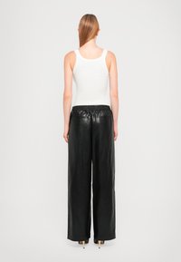 Sorte lærbukser med vide ben, elastisk talje, glat tekstur og to baglommer. Sættes sammen med en hvid tanktop.