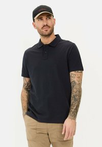 Mørkeblå kortærmet polo-shirt med en tre-knap lukkefront og et subtilt brandlogo. Har en glat stofstruktur. Ingen synlige mønstre.