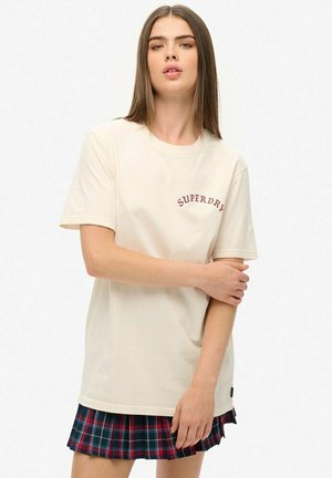 Beżowa bawełniana koszulka z krótkim rękawem, z czerwonym haftowanym logo "SUPERDRY". W zestawie z plisowaną mini spódnicą w kratę w ciemnych odcieniach.